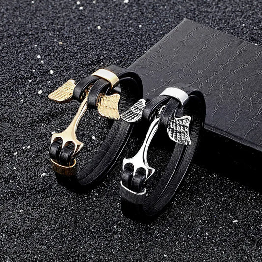 Black leather bracelets with gold and silver winged charms on a dark textured surface.