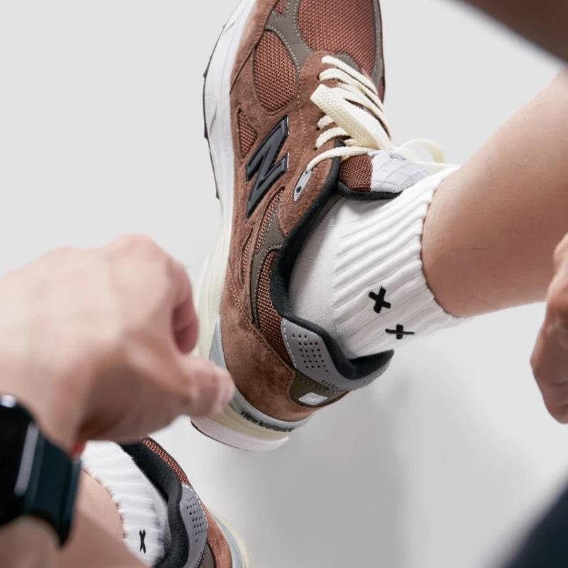 Brown and white sneakers with a person adjusting them on a light background